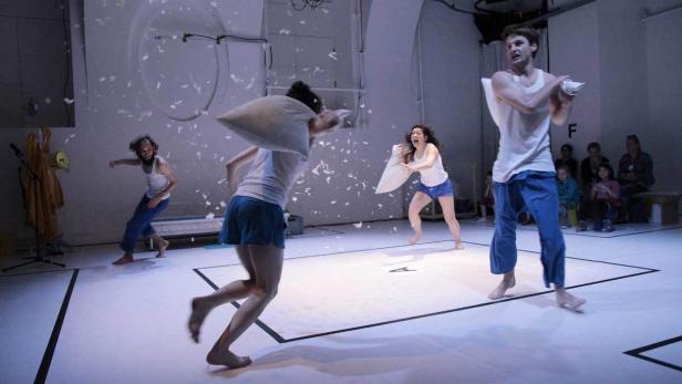 Mehrere Personen in lässiger Kleidung liefern sich eine Kissenschlacht auf einer Bühne.