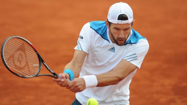Ein Tennisspieler schlägt einen Ball auf einem Sandplatz.