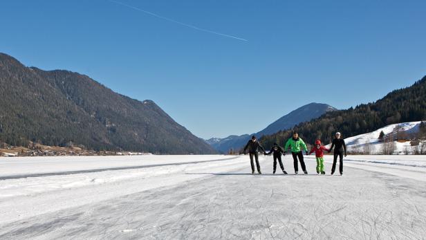 Eine Familie läuft Hand in Hand auf einem zugefrorenen See Schlittschuh.