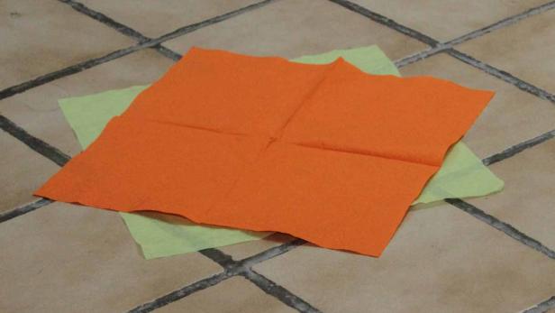 Zwei Servietten, eine orange und eine hellgrün, liegen auf einem Fliesenboden.