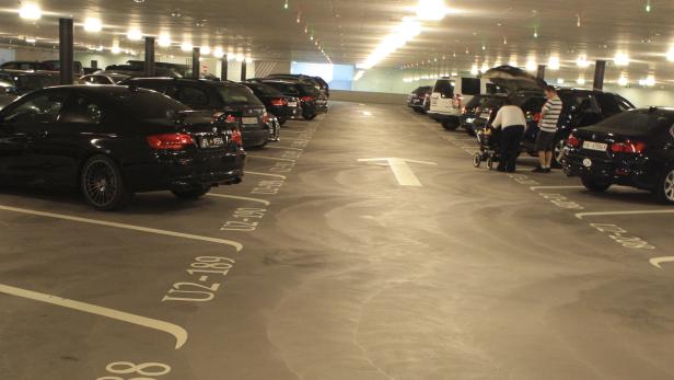 Eine Tiefgarage mit geparkten Autos und Personen mit einem Kinderwagen.