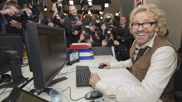 Thomas Gottschalk sitzt am Schreibtisch, während er von Fotografen umringt ist.