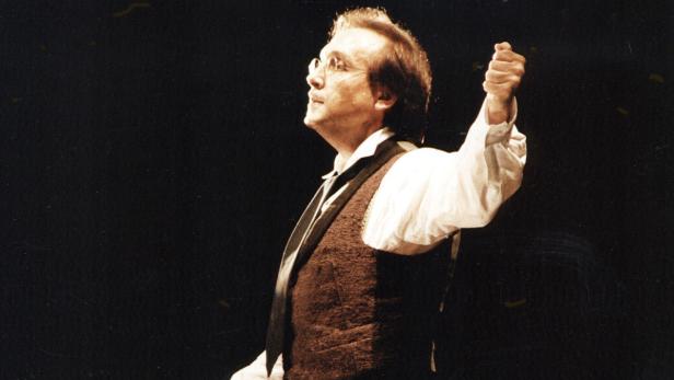 Ein Mann mit Brille und Weste dirigiert ein Orchester.