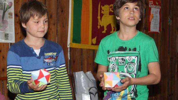 Zwei Jungen halten bunte, geometrische Papierobjekte in ihren Händen.