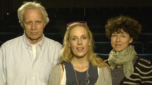 Drei Personen stehen vor leeren Sitzen in einem Theater.