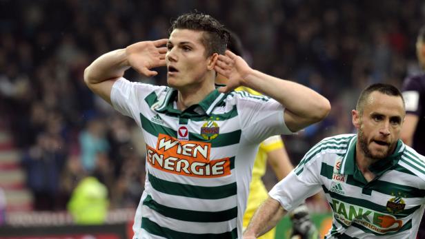 Ein Fußballspieler von Rapid Wien jubelt mit erhobenen Händen vor dem Publikum.