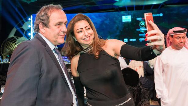 Eine Frau macht ein Selfie mit Michel Platini bei einer Veranstaltung.