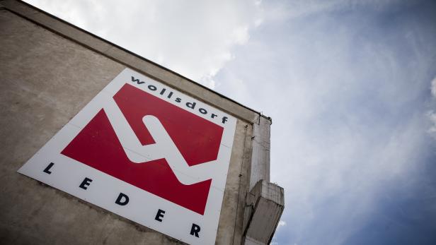 Das Logo von Wollsdorf Leder an einer Gebäudewand unter blauem Himmel.