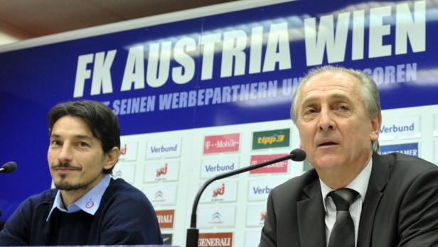 Zwei Männer sitzen vor einem Banner des FK Austria Wien bei einer Pressekonferenz.