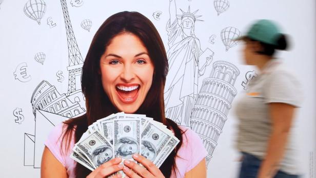 Eine Frau freut sich über einen Stapel US-Dollar vor einer Wand mit Sehenswürdigkeiten.