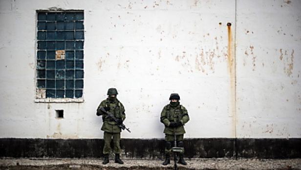 Zwei Soldaten stehen vor einer weissen Wand mit einem vergitterten Fenster.