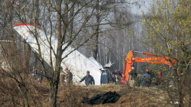 Ein Flugzeugwrack liegt in einem Wald, während Rettungskräfte und ein Bagger vor Ort sind.