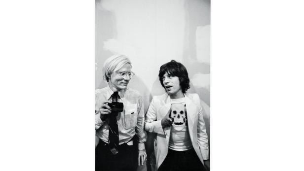 Andy Warhol und Mick Jagger posieren zusammen, Warhol mit einer Kamera, Jagger mit einem Totenkopf.