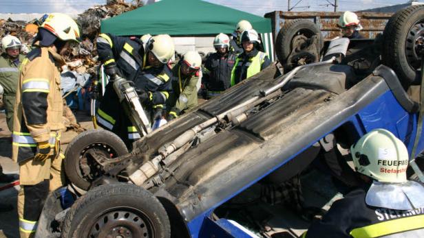 Feuerwehrleute arbeiten an einem auf dem Dach liegenden blauen Auto.