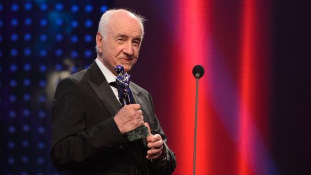 Ein Mann im Anzug hält eine Auszeichnung auf einer Bühne.