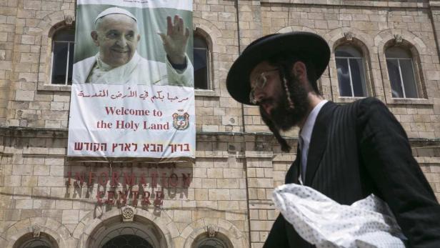 Ein orthodoxer Jude geht an einem Banner mit einem Bild von Papst Franziskus in Jerusalem vorbei.