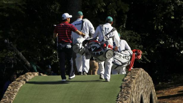 Ein Golfer und seine Caddies überqueren eine kleine Brücke auf einem Golfplatz.