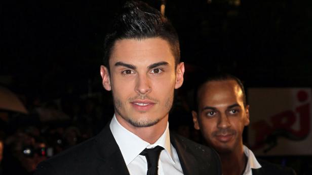 Ein Mann im Anzug mit einem weiteren Mann im Hintergrund.