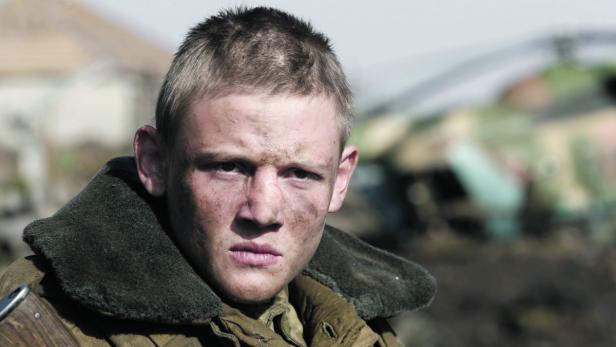 Ein junger Soldat mit Schmutz im Gesicht blickt ernst in die Kamera.