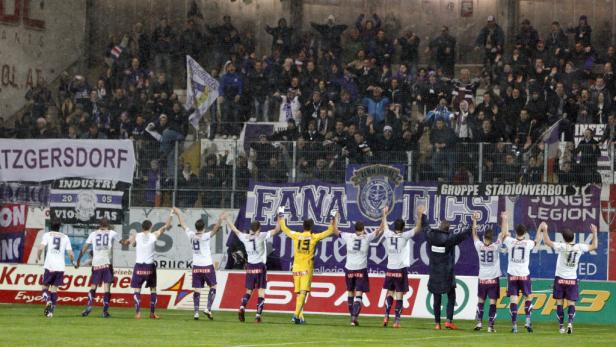 Fußballspieler feiern vor einer Tribüne voller Fans im Stadion.