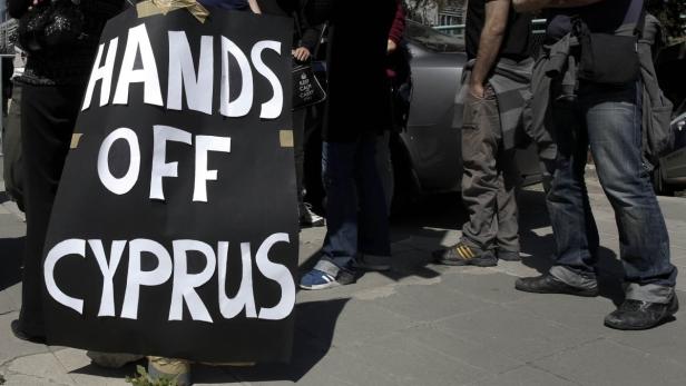 A group of demonstrators hold an anti-bailout rally outside the parliament in Nicosia March 18, 2013. Cypriot ministers rushed on Monday to revise a plan to seize money from bank deposits as part of an EU bailout, in an effort to ensure lawmakers supported it in a vote later in the day. The weekend announcement that Cyprus would impose a tax on bank accounts as part of a 10 billion euro ($13 billion) bailout broke with previous practice that depositors&#039; savings were sacrosanct and sent a shiver across the bloc, causing the euro to tumble and stock markets to dive. REUTERS/Yorgos Karahalis (CYPRUS - Tags: POLITICS CIVIL UNREST BUSINESS)