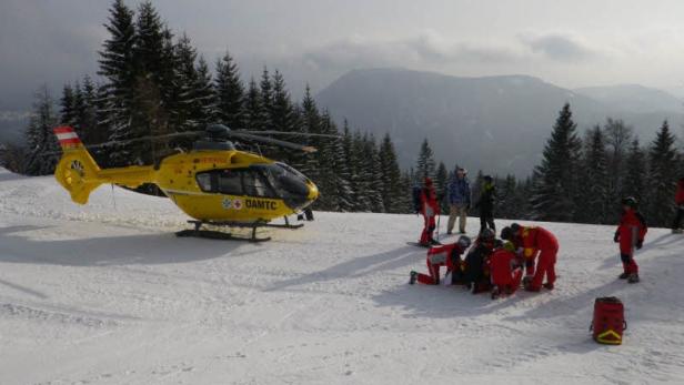 Ein gelber Rettungshubschrauber des ÖAMTC steht auf einer schneebedeckten Bergwiese.