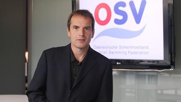 Ein Mann im Anzug steht vor einem Bildschirm mit dem Logo des Österreichischen Schwimmverbandes (OSV).