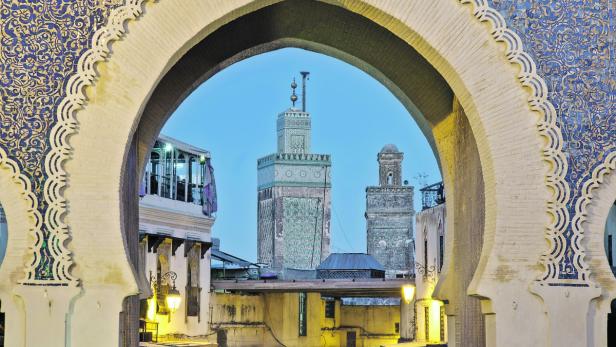 Blick durch einen verzierten Torbogen auf die Altstadt von Fès, Marokko.