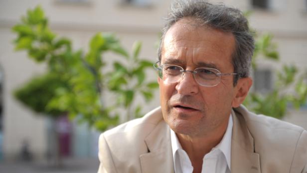 Ein Mann mit Brille und hellem Sakko sitzt im Freien.