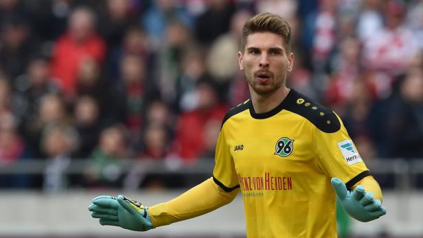 Ein Torwart von Hannover 96 in gelber Spielkleidung und hellblauen Handschuhen vor einer Zuschauermenge.