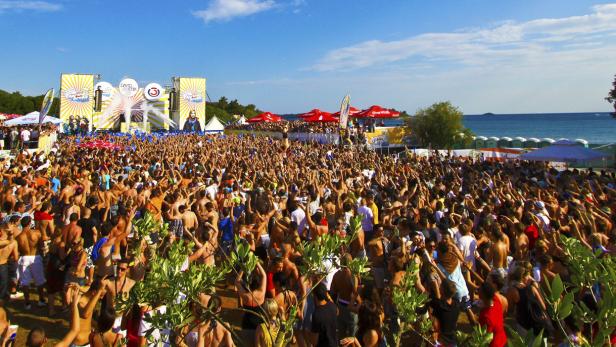 Eine große Menschenmenge feiert bei einem Open-Air-Konzert am Strand.