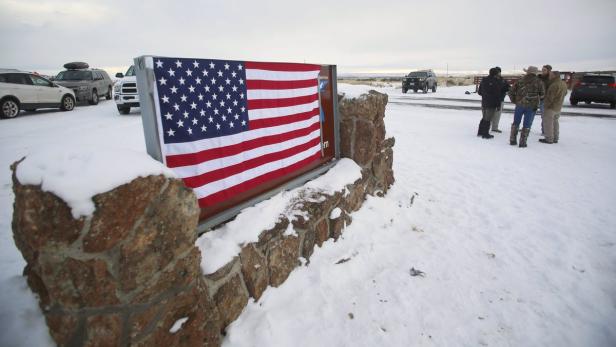 Eine amerikanische Flagge an einem steinernen Denkmal im Schnee, umgeben von einer Gruppe von Menschen und Autos.