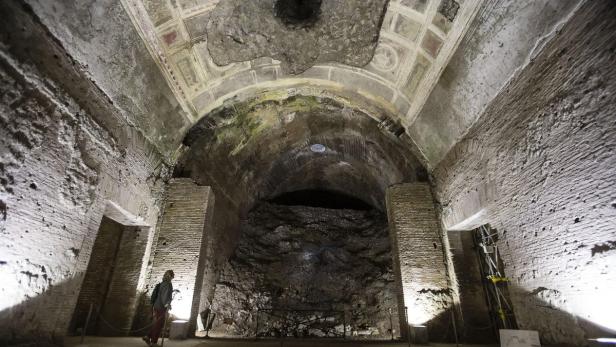 Eine Person steht in einem alten, gewölbeartigen Raum mit Ziegelwänden und Deckenmalereien.