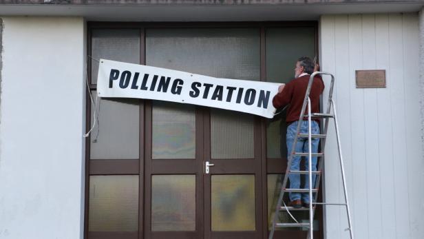 Ein Mann befestigt ein Schild mit der Aufschrift „Polling Station“ an einem Gebäude.