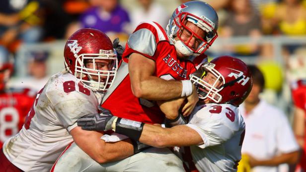 Drei American-Football-Spieler kämpfen um den Ball.