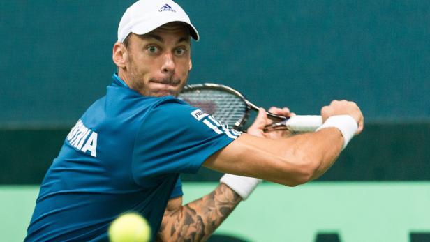 Ein Tennisspieler mit Tätowierung am Arm schlägt einen Ball.
