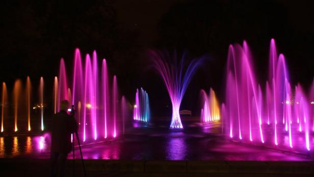 Ein Fotograf macht nachts Aufnahmen von einem farbig beleuchteten Springbrunnen.