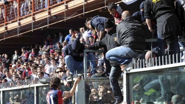 Fußballfans klettern über eine Absperrung im Stadion.