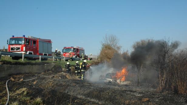 Feuerwehrleute löschen einen Brand neben zwei roten Feuerwehrfahrzeugen.