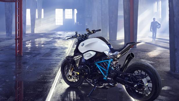 Ein weißes BMW-Motorrad steht in einer Lagerhalle, im Hintergrund eine Person mit Helm.