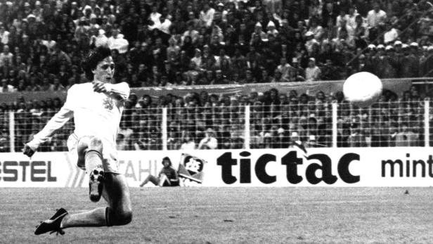 Ein Fußballspieler schießt vor einer Zuschauermenge einen Ball.