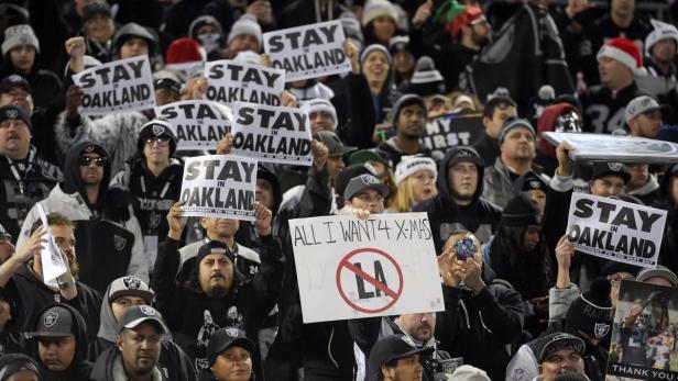 Eine Menschenmenge hält Schilder mit der Aufschrift „Stay in Oakland“ bei einem Raiders-Spiel hoch.