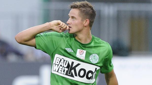 Ein junger Mann im grünen Trikot mit Sponsorenlogo kaut auf seinen Fingernägeln.