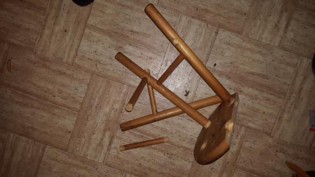 Ein kaputter, hölzerner Hocker liegt auf dem Boden.