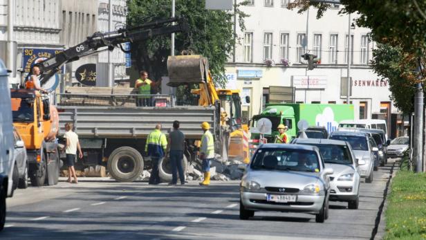 Bauarbeiter sind mit einem Bagger auf einer belebten Straße im Einsatz.