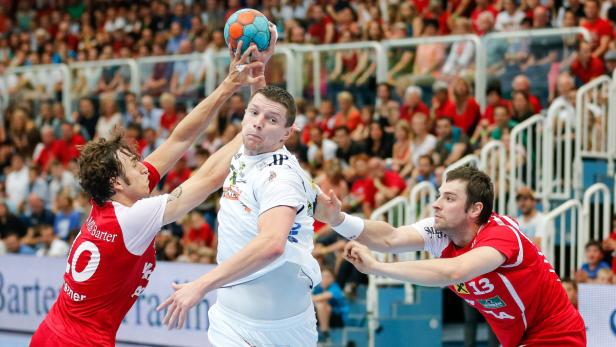 Ein Handballspieler wird von zwei Gegenspielern während eines Spiels bedrängt.