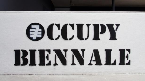 Auf einer Wand steht in schwarzer Schrift „Occupy Biennale“.