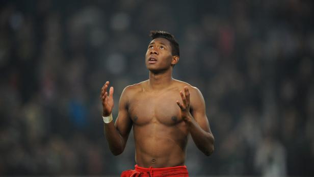 Ein barfüßiger Mann mit roter Hose blickt mit erhobenen Händen nach oben.