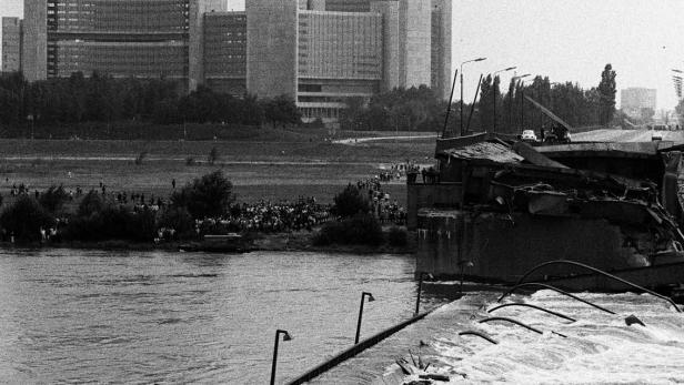 Eine eingestürzte Brücke, auf der ein Bus steht, mit einem Rettungsboot in reißendem Wasser.