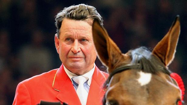 Ein Mann in roter Jacke steht neben dem Kopf eines Pferdes.